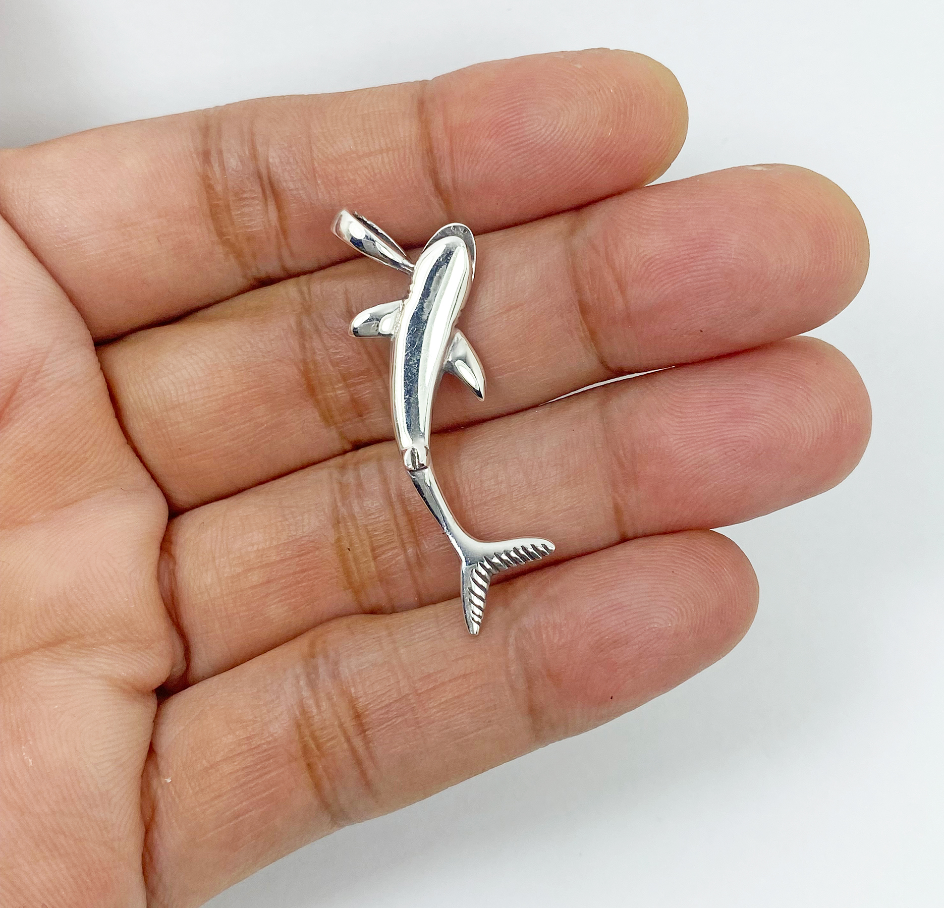 A detailed macro shot showing a handcrafted 3D solid 925 sterling silver shark pendant held in an open palm, highlighting its sleek, high-polished finish back side view.