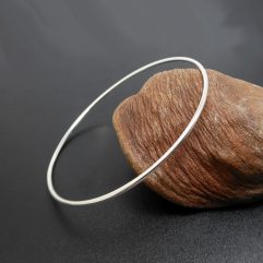 A simple and elegant 925 sterling silver solid round bangle, displayed next to a decorative seed pod.