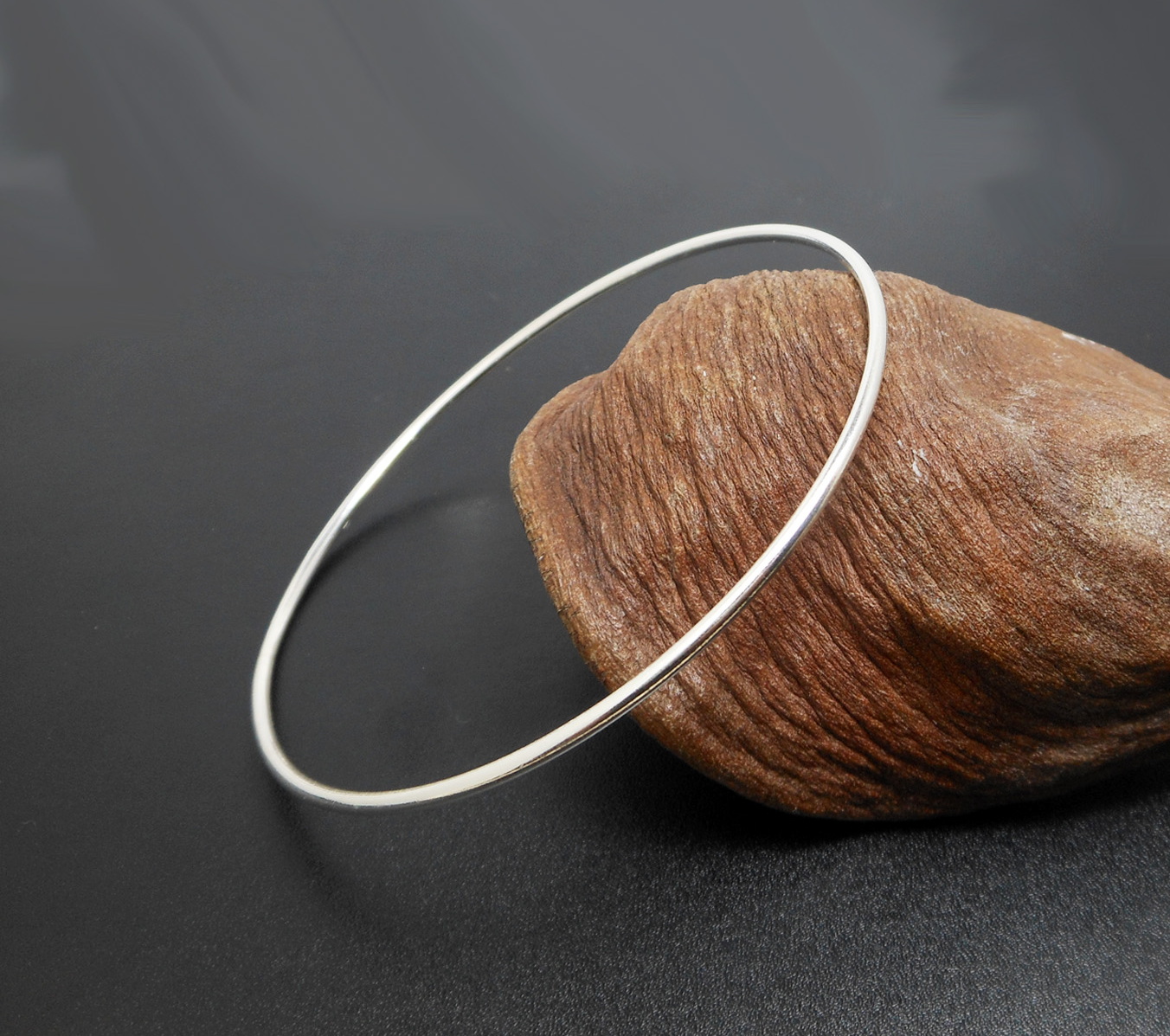 A simple and elegant 925 sterling silver solid round bangle, displayed next to a decorative seed pod.