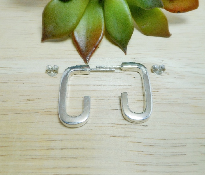 A pair of handcrafted 925 sterling silver puffy rectangle tube hoop stud earrings featuring a high-polished, sleek, and architectural 3D design, displayed on a wooden surface.