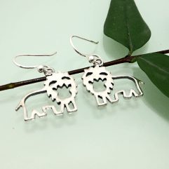 A pair of handcrafted 925 sterling silver smiling cutout lion drop earrings displayed on a thin green branch with leaves
