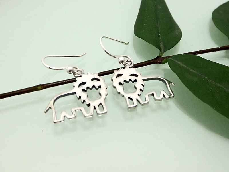 A pair of handcrafted 925 sterling silver smiling cutout lion drop earrings displayed on a thin green branch with leaves