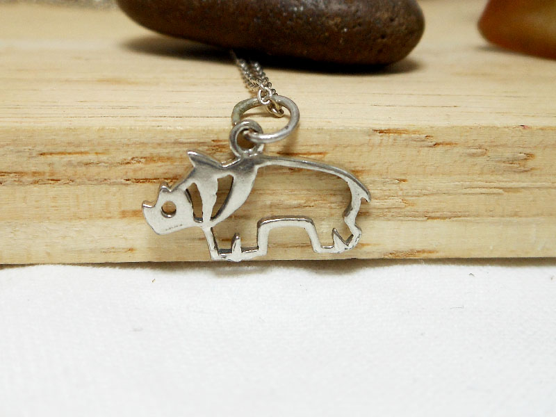 A close-up shot of a handcrafted 925 sterling silver cutout rhinoceros pendant on a delicate chain, resting against a weathered wood background.