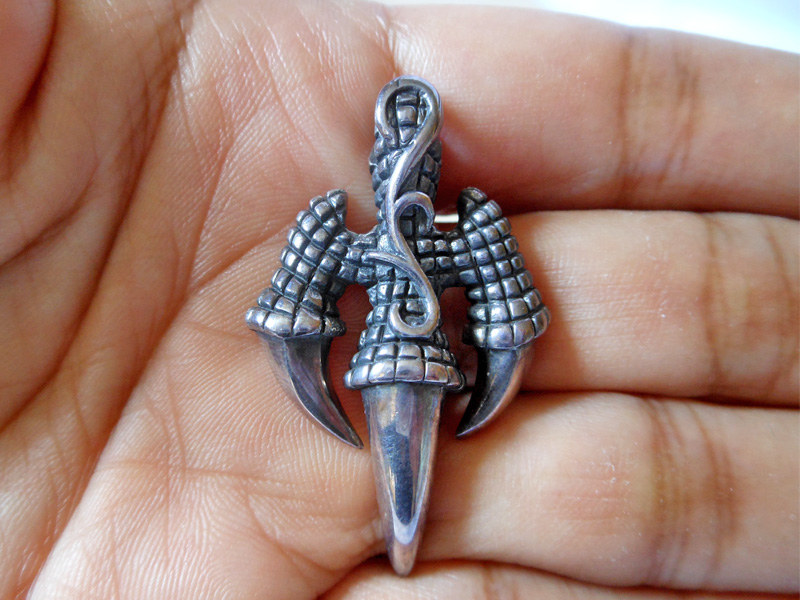 A detailed macro photograph of a handcrafted, oxidized 925 sterling silver eagle claw pendant resting on an open palm