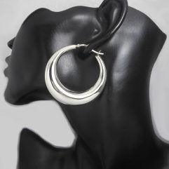 A pair of large, chunky 925 sterling silver puffy hoop earrings (50mm) shown on a black mannequin display and laid out on a clean surface.