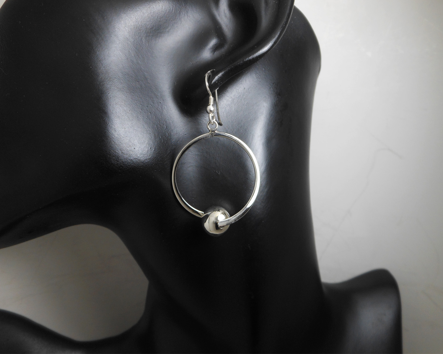 A pair of handcrafted 925 sterling silver drop earrings featuring a circular frame with a polished silver bead, displayed on a jewelry mannequin.