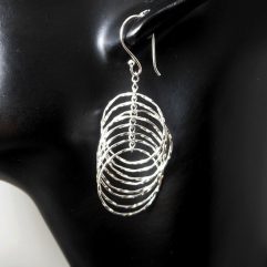 A pair of handcrafted 925 sterling silver multi diamond-cut edge layered hoop drop earrings displaying a brilliant spinning textured finish on a display mannequin.