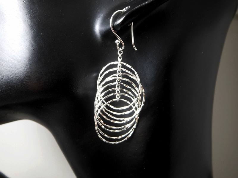 A pair of handcrafted 925 sterling silver multi diamond-cut edge layered hoop drop earrings displaying a brilliant spinning textured finish on a display mannequin.
