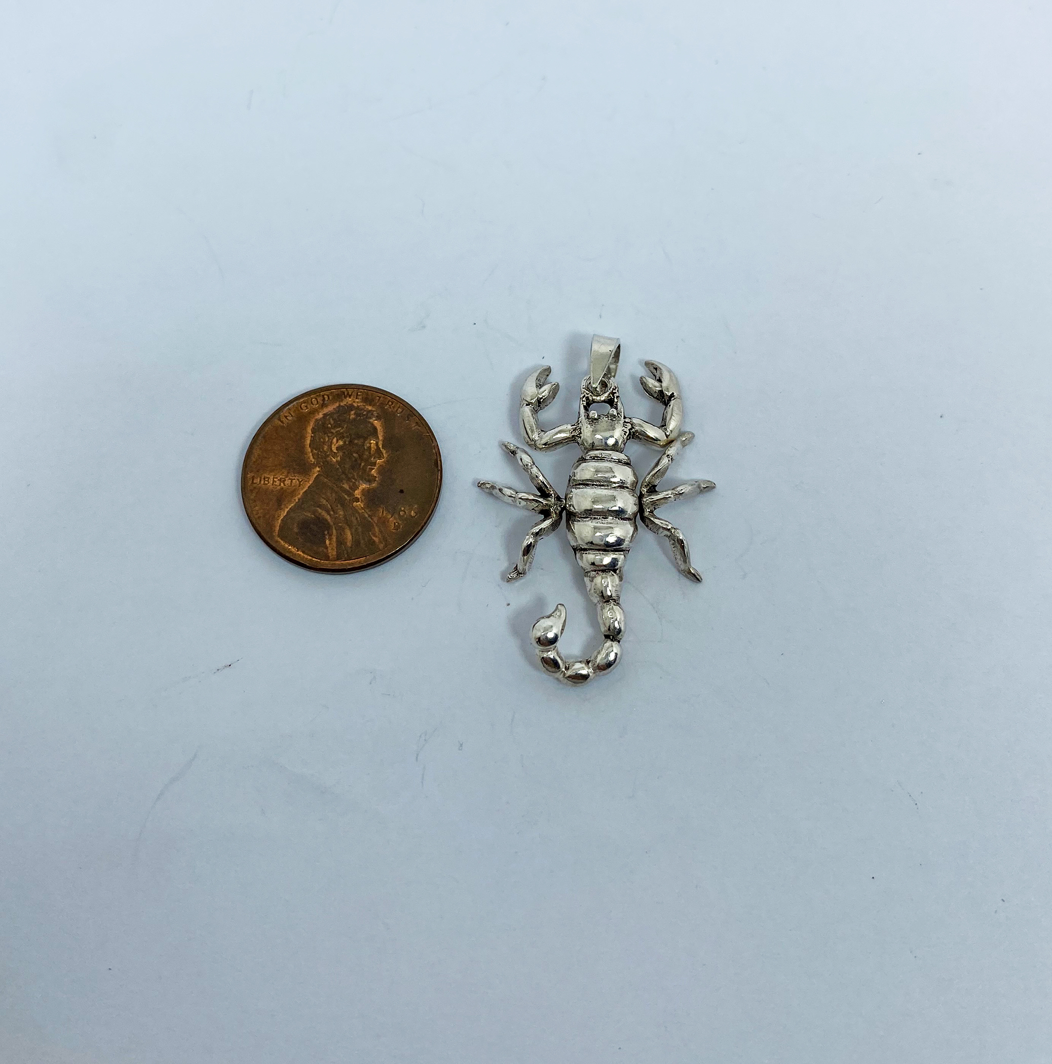 A detailed macro shot of a handcrafted 3D 925 sterling silver scorpion pendant with movable parts, shown next to a US penny for scale.