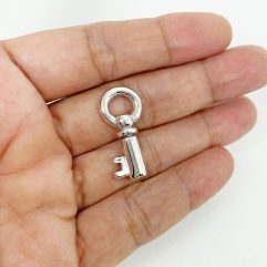 A detailed macro shot showing a solid, high-polished 3D prison key pendant made of 925 sterling silver, resting on a dark stone and held in an open palm.