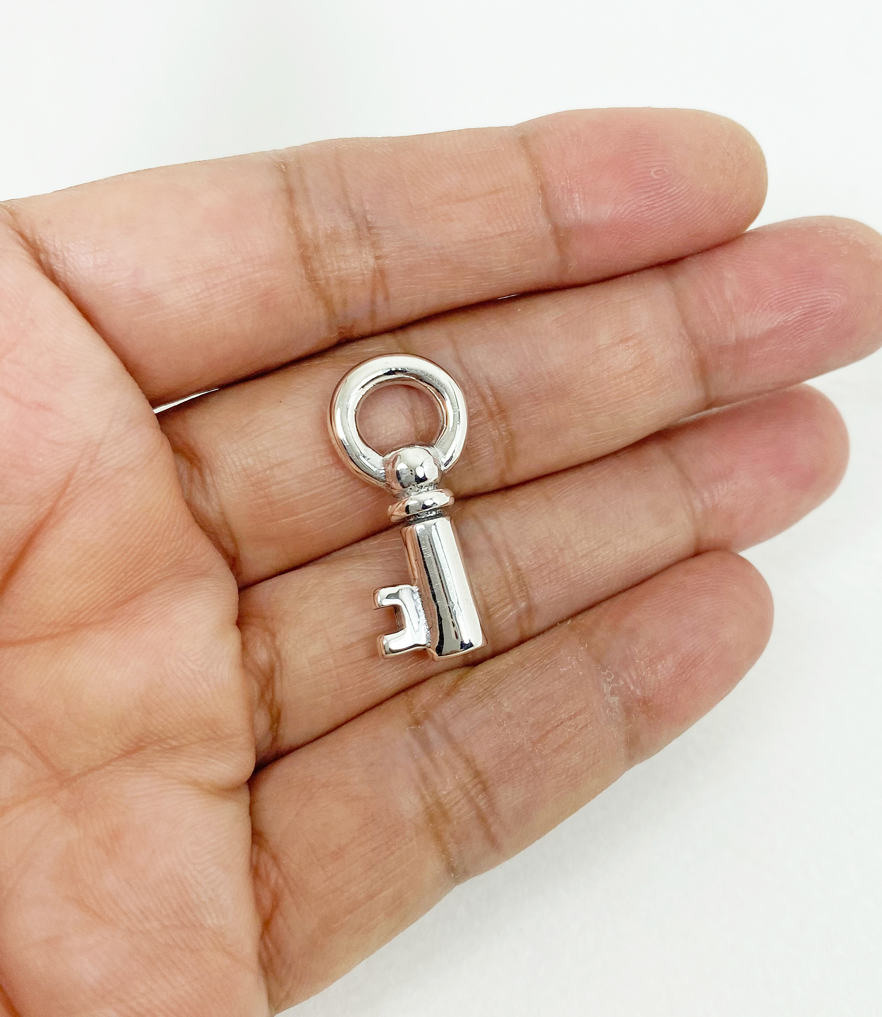 A detailed macro shot showing a solid, high-polished 3D prison key pendant made of 925 sterling silver, resting on a dark stone and held in an open palm.