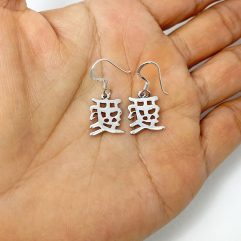 A pair of handcrafted 925 sterling silver drop earrings featuring the Chinese character for "Love" in a smooth, high-polished, and solid cutout design, displayed on a hand.