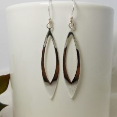 A pair of handcrafted 925 sterling silver open leaf drop earrings with a sleek, high-polished finish, shown on a white display stand.