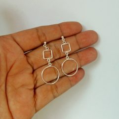 A pair of handcrafted 925 sterling silver drop earrings featuring an open square connected to an open circle, displayed in a hand.