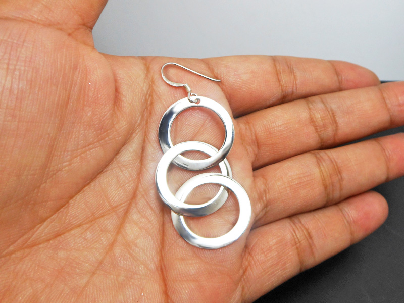 A pair of handcrafted 925 sterling silver drop earrings featuring three interconnected smooth, high-polished circles, displayed in a hand.