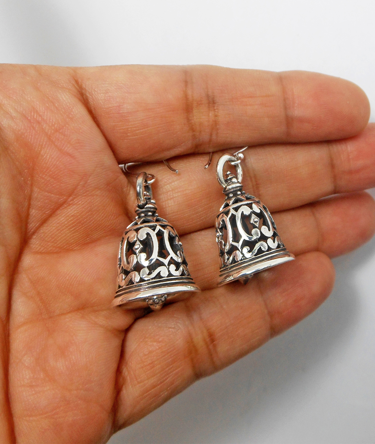 A pair of handcrafted 925 sterling silver bell-shaped drop earrings featuring intricate Thai art textured patterns and a high-polished oxidized finish, displayed in a hand.