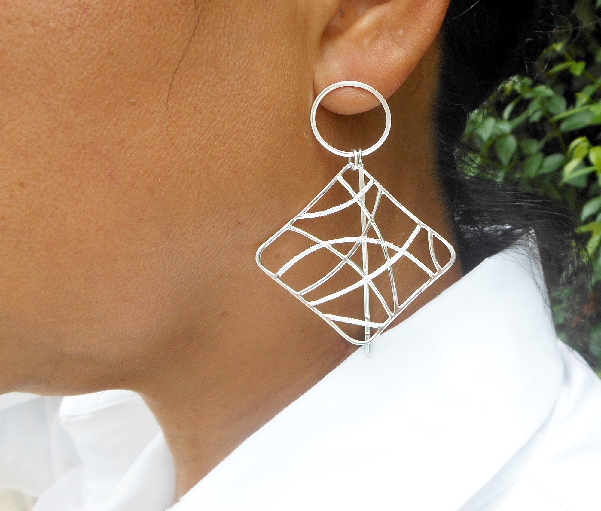 A pair of large, handcrafted 925 sterling silver geometric web dangle earrings featuring a mix of polished and sandy textures, displayed on a model.