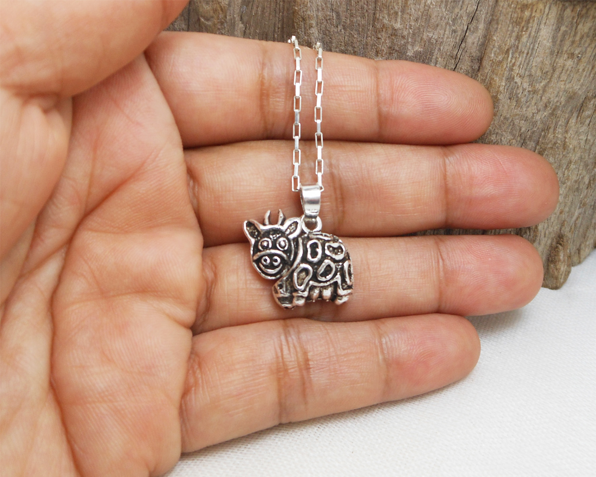A detailed photograph of a handcrafted 925 sterling silver cow pendant with a movable design and textured finish, shown held in a palm.