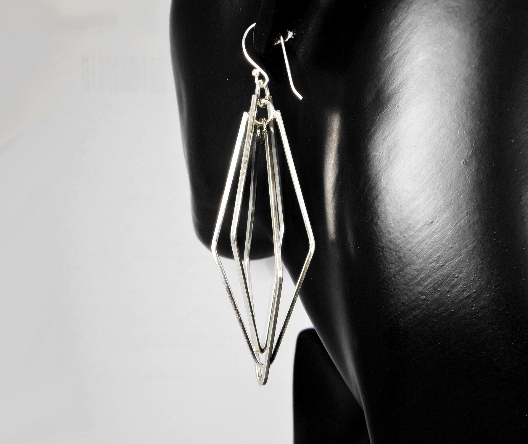A pair of handcrafted 925 sterling silver spinning rhombus geometric drop earrings displayed on a black mannequin, highlighting their multi-layered design.