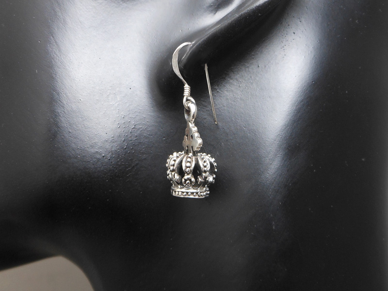 A hand holding a small, detailed 925 sterling silver textured royal crown drop earring with an oxidized and shiny finish.
