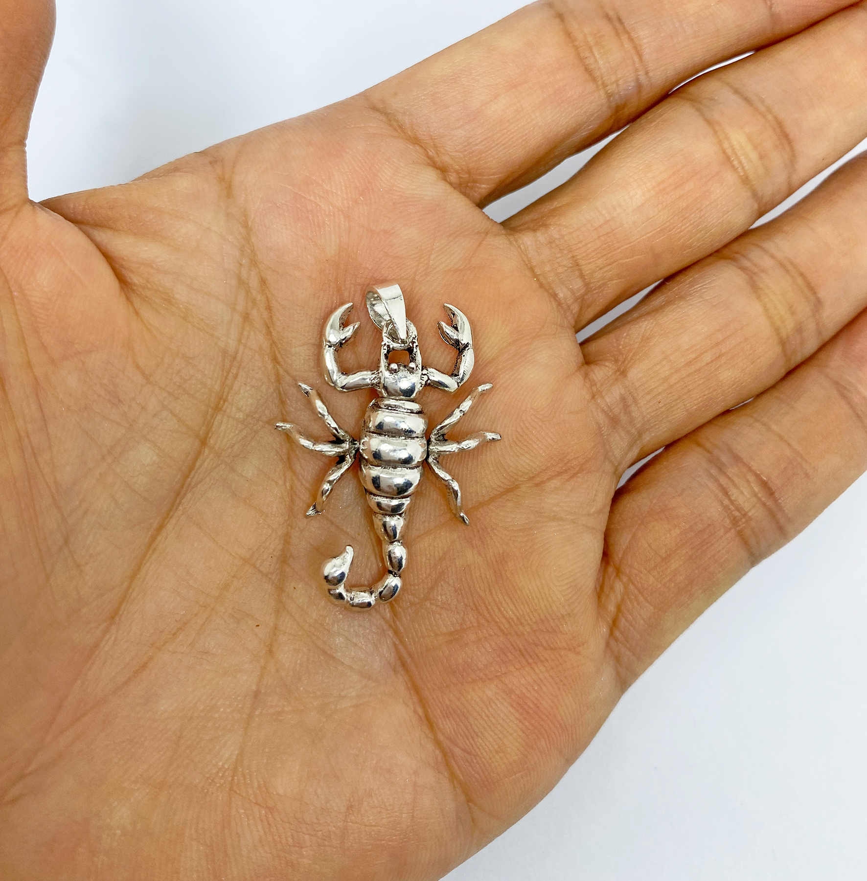 A detailed macro shot of a handcrafted 3D 925 sterling silver scorpion pendant with movable parts, displayed resting on an open palm.