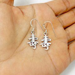 A pair of handcrafted 925 sterling silver drop earrings featuring the Chinese character for "Long Life" in a polished, solid cutout design, held in a hand.