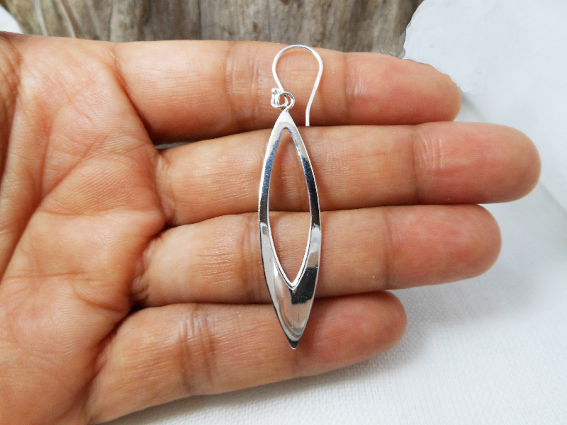A pair of handcrafted 925 sterling silver open leaf drop earrings with a sleek, high-polished finish, shown in hand.