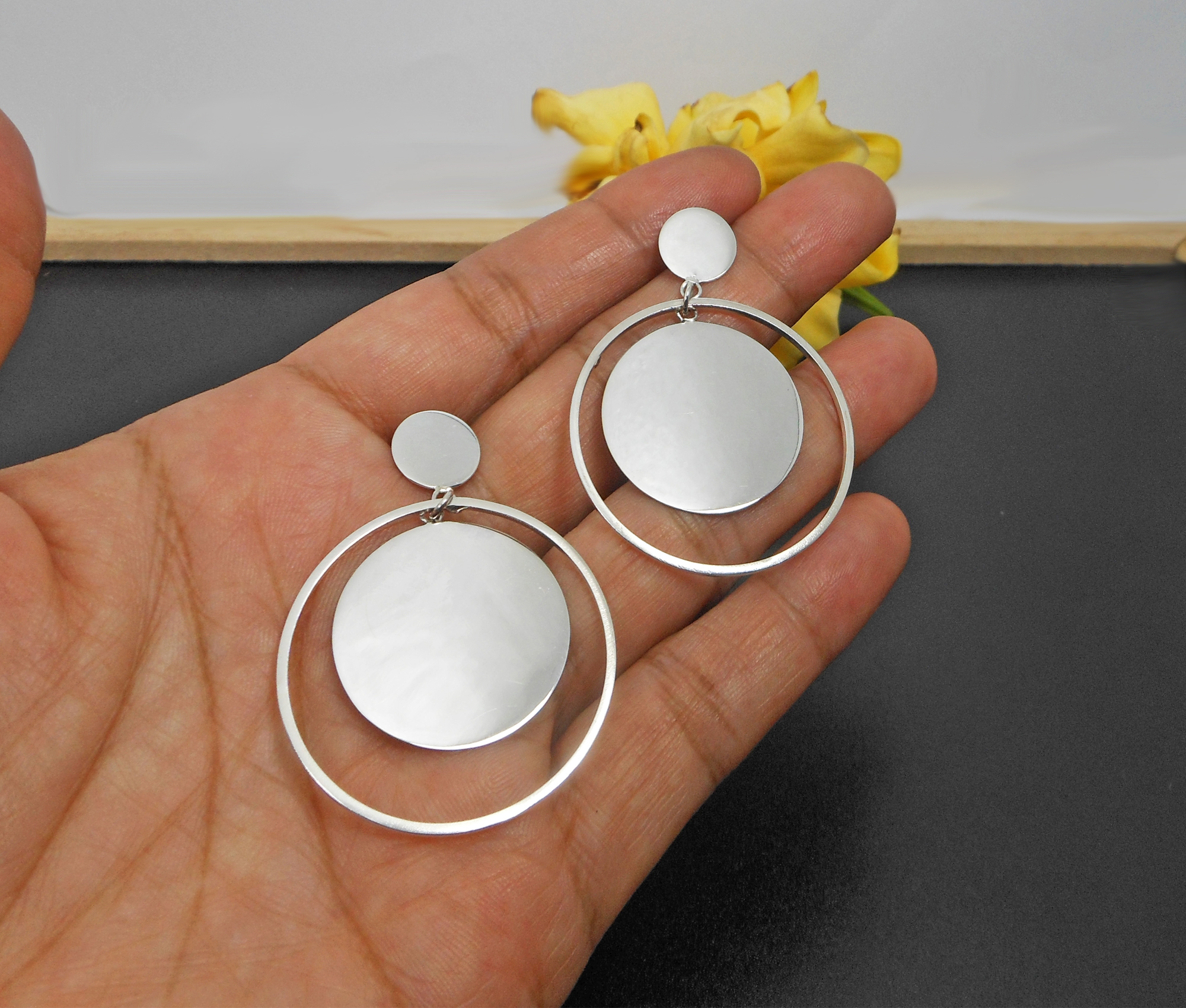 A pair of handcrafted 925 sterling silver drop earrings featuring a spinning inner round disc within an outer circle, displayed in a hand.
