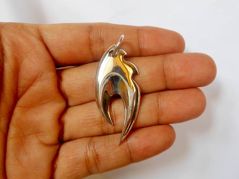 A macro shot of a sleek, high-polished 925 sterling silver fire flame pendant held in an open palm.