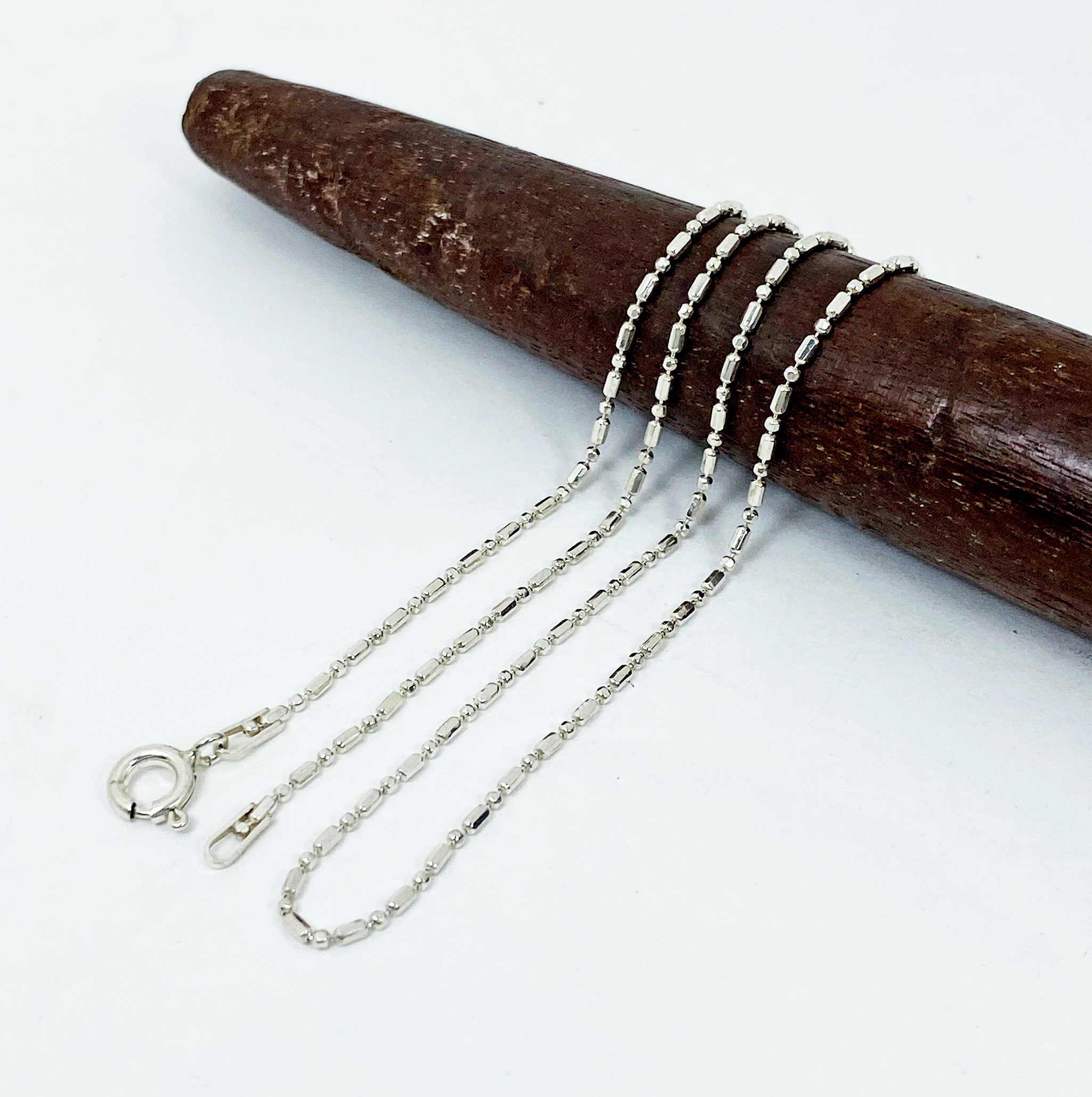 A macro shot of a delicate, high-polished 925 sterling silver fancy cutting beads chain necklace, displayed on a textured wood surface.
