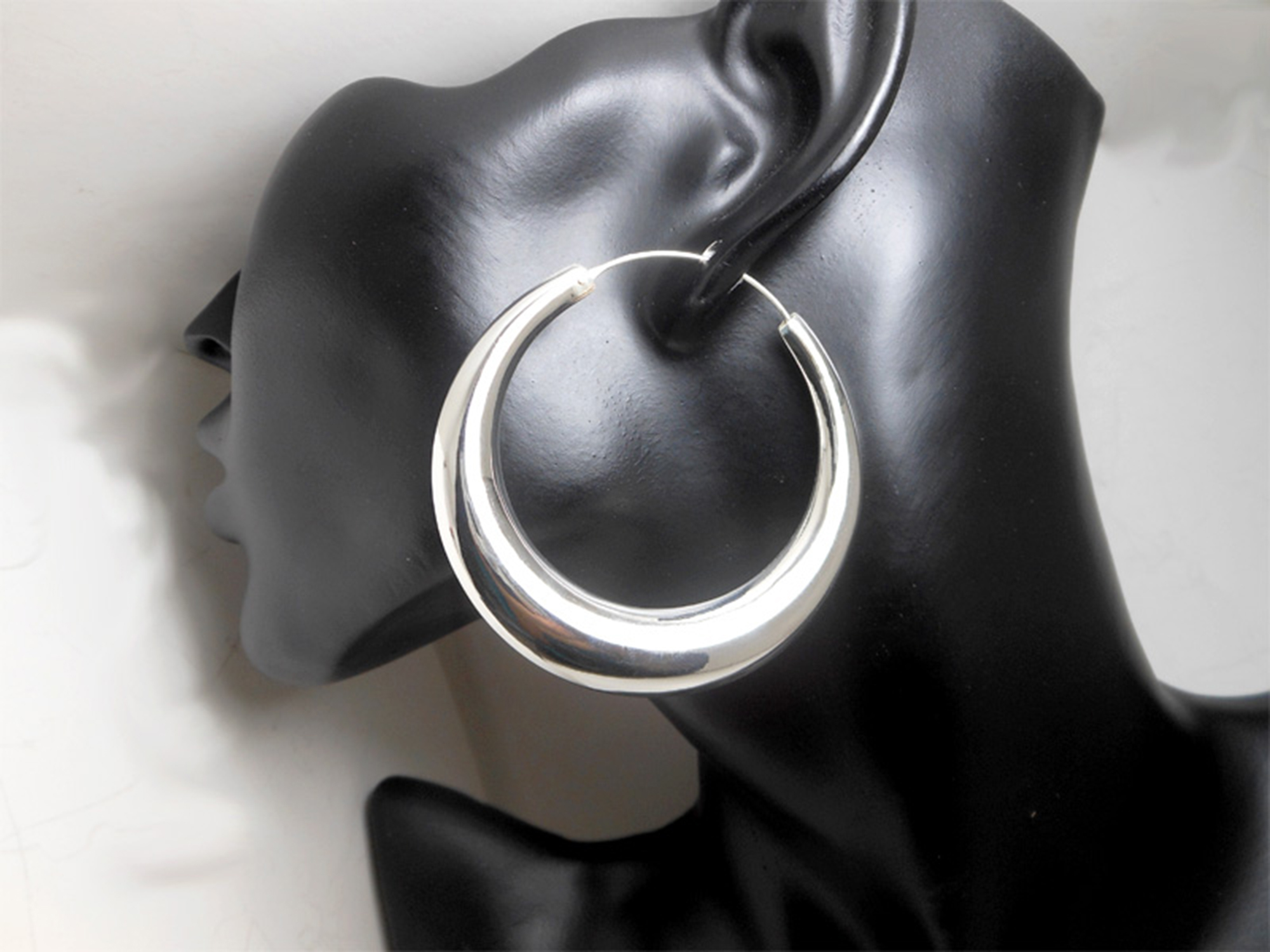 A pair of handcrafted 925 sterling silver puffy tribal chubby hoop earrings held in a hand, showcasing their bold, high-polished, and smooth sculptural form.