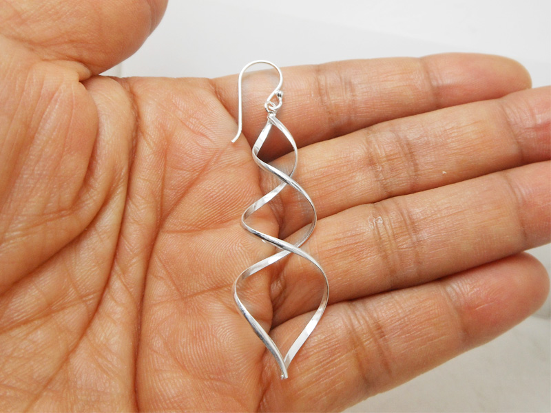 A pair of handcrafted 925 sterling silver spiral dangle earrings featuring an elegant twist design and a high-polished smooth finish, displayed in a hand.