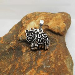 A detailed photograph of a handcrafted 925 sterling silver cow pendant with a movable design and textured finish, resting on a rustic stone surface.