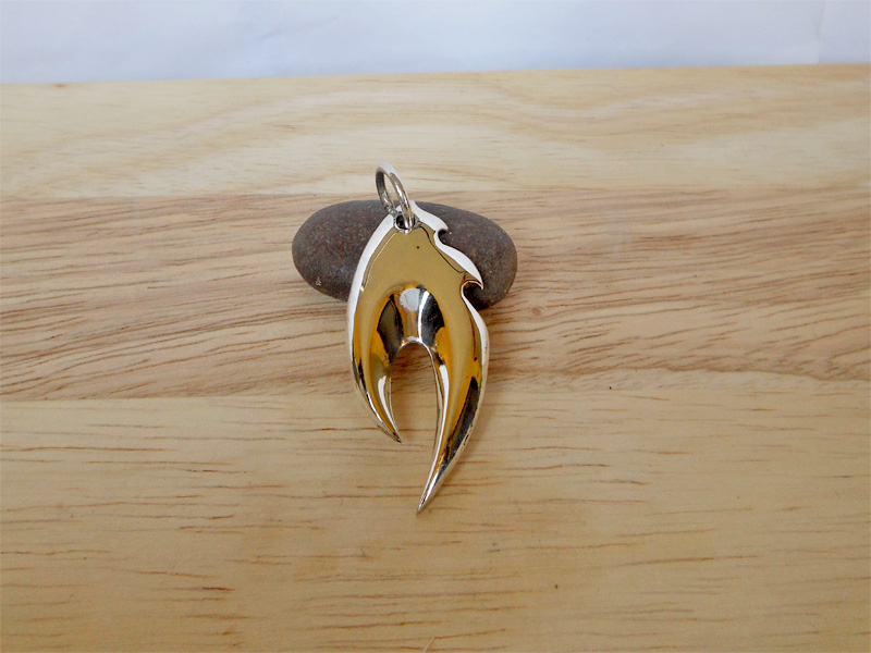 A macro shot of a sleek, high-polished 925 sterling silver fire flame pendant resting on a natural stone surface.
