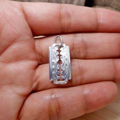 A detailed macro photograph showing a textured, handcrafted 925 sterling silver razor blade pendant held in an open palm.