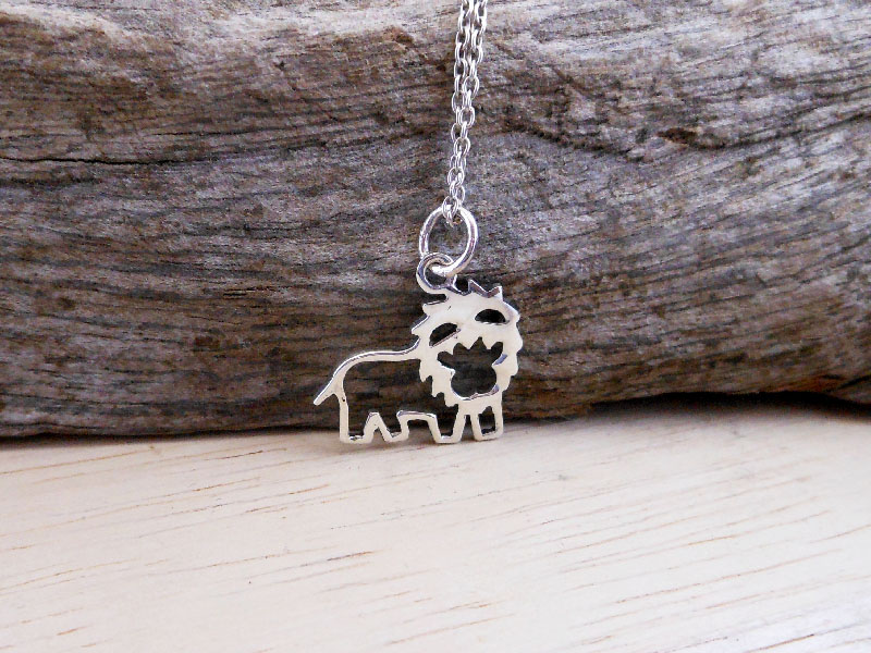 A detailed close-up of a handcrafted 925 sterling silver cutout lion pendant necklace displayed against a natural wood background.