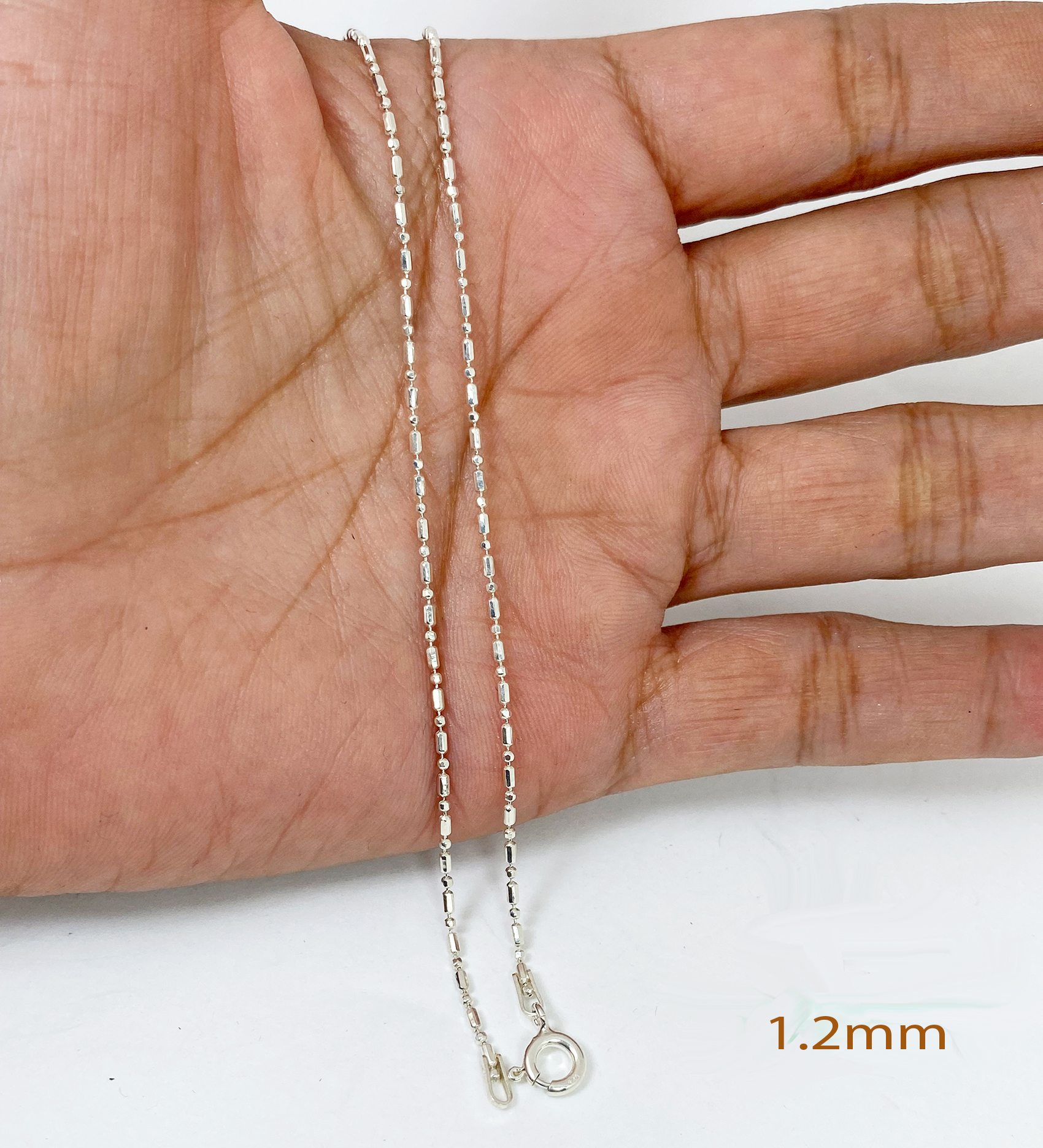 A macro shot of a delicate, high-polished 925 sterling silver fancy cutting beads chain necklace, displayed held in an open palm to show its intricate texture and 1.2mm width.
