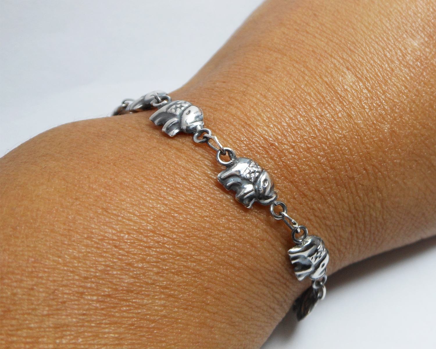 A detailed close-up of a handcrafted 925 sterling silver bracelet featuring a series of tiny puffed elephant charms linked together, wearing on modeled
