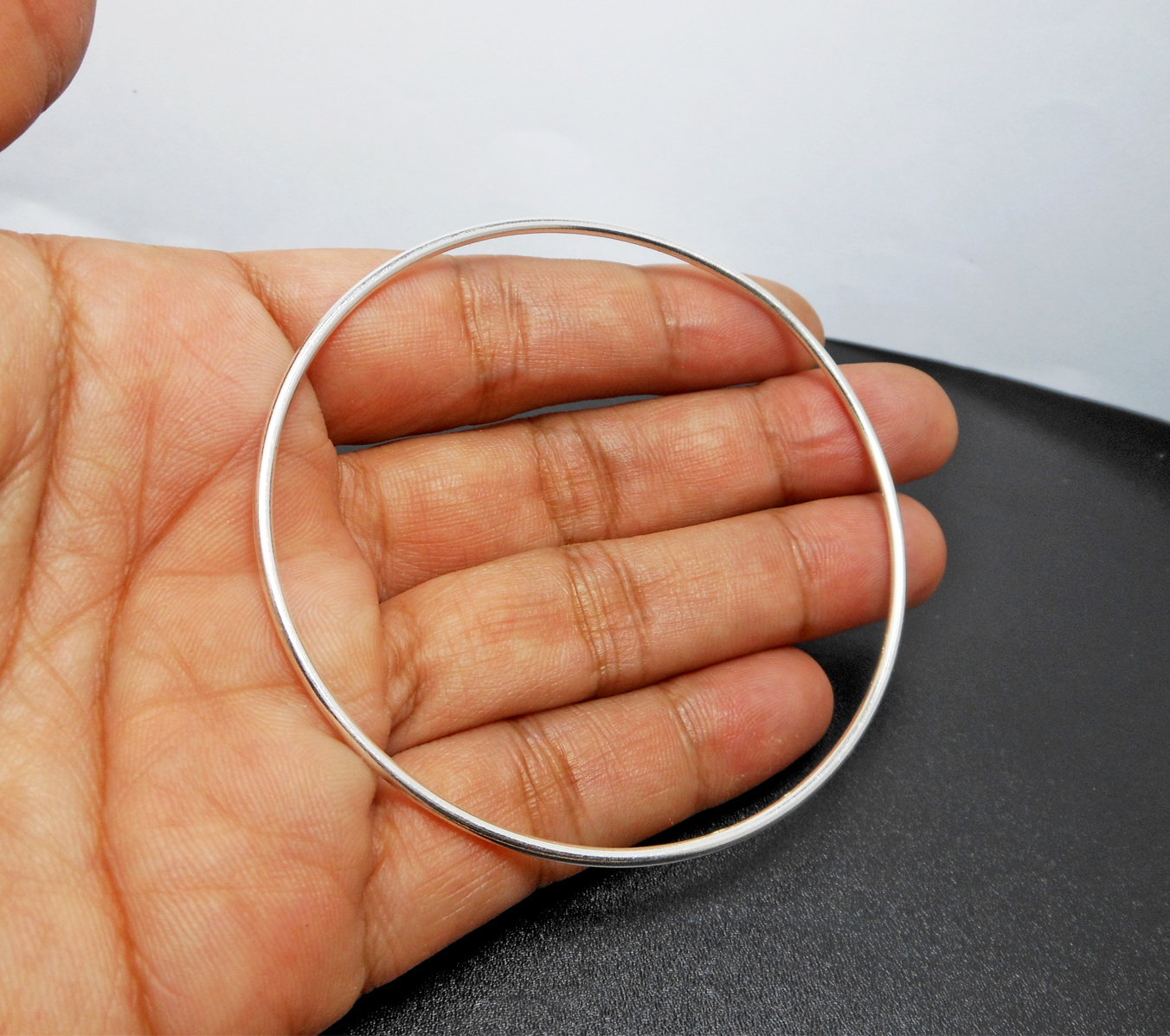 A simple and elegant 925 sterling silver solid round bangle, being held in a palm to show its thin 1.5mm profile.