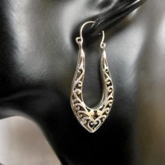 A pair of handcrafted 925 sterling silver long hoop earrings featuring intricate, perforated heart-shaped filigree patterns, displayed on a black mannequin.