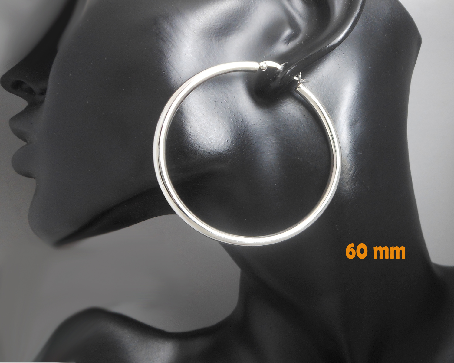 A pair of handcrafted 925 sterling silver large 60mm round hoop earrings featuring a smooth, high-polished wide tube design, displayed on a black mannequin.