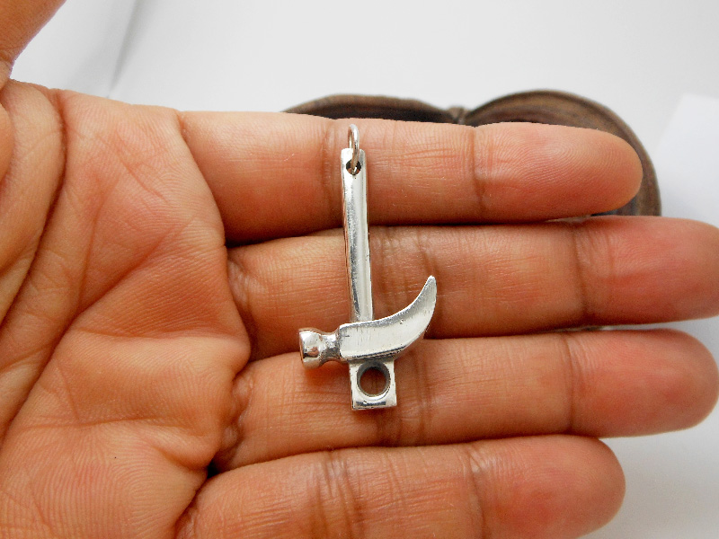 A detailed macro shot of a handcrafted 3D 925 sterling silver hammer pendant featuring a smooth, polished finish, held against an open palm