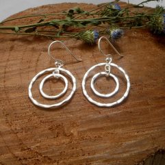 A pair of handcrafted 925 sterling silver drop earrings featuring two interlocking circles with a hammered, organic texture and a high-polished finish.