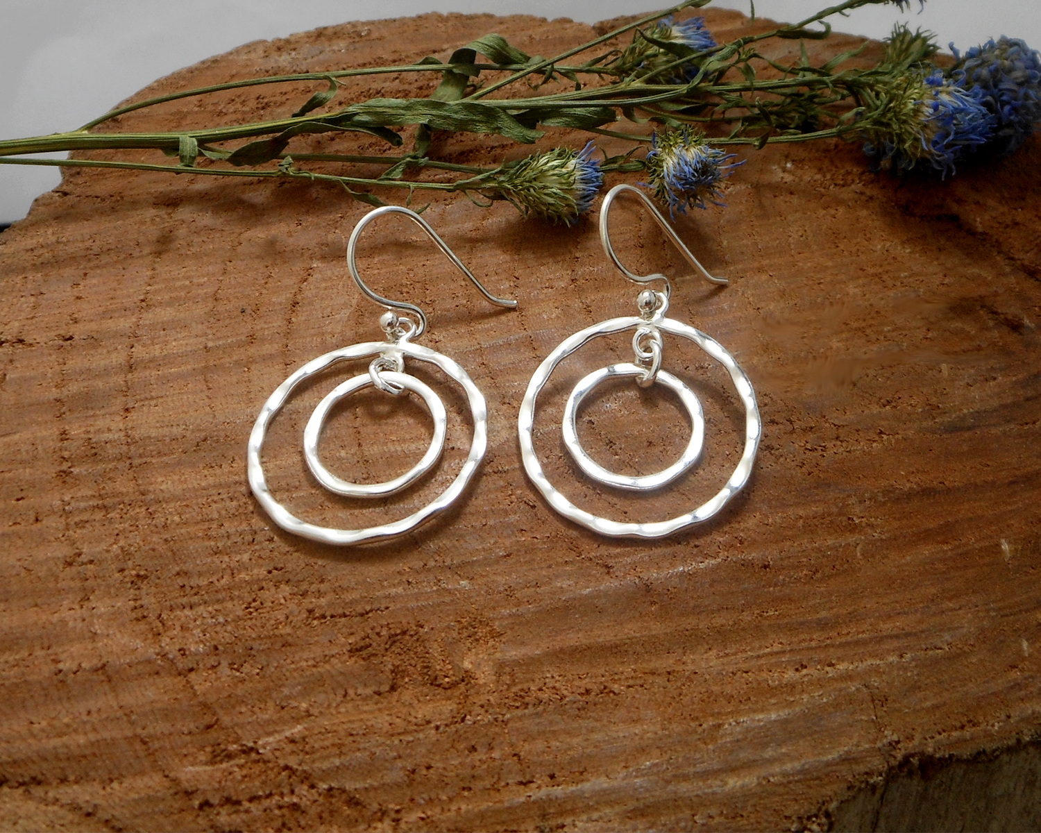 A pair of handcrafted 925 sterling silver drop earrings featuring two interlocking circles with a hammered, organic texture and a high-polished finish.