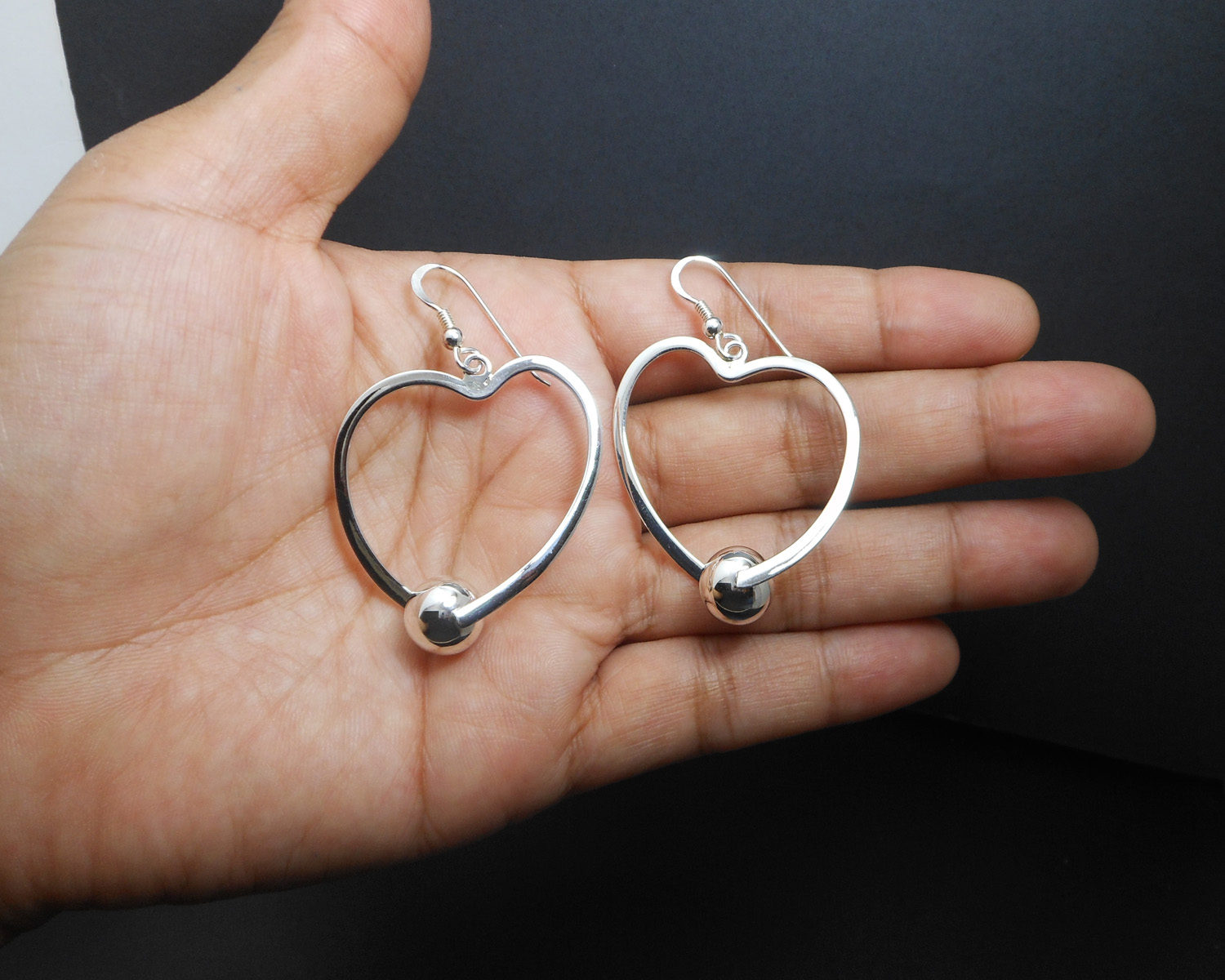 A pair of handcrafted 925 sterling silver open heart drop earrings featuring a unique polished spinning bead, perfect for Valentine's Day.