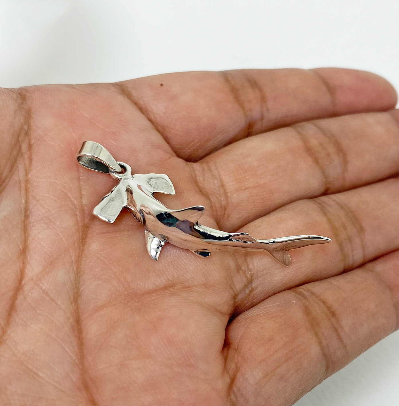A detailed macro shot showing a handcrafted 3D solid 925 sterling silver swimming hammerhead shark pendant held in an open palm, displaying its polished finish.