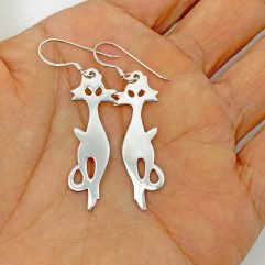 A pair of handcrafted 925 sterling silver cat-shaped dangle earrings with a high-polished, smooth finish, held in a hand.