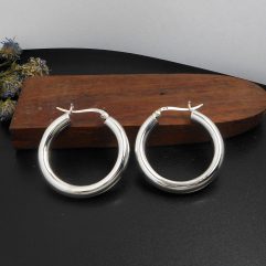 A pair of handcrafted 30mm 925 sterling silver round hoop earrings with a 5mm tube width, displayed near a wooden block, showcasing their high-polished, smooth surface.