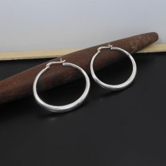 A pair of handcrafted 925 sterling silver tapered ellipse hoop earrings held in a hand, showcasing their smooth, high-polished, and puffed sculptural design.
