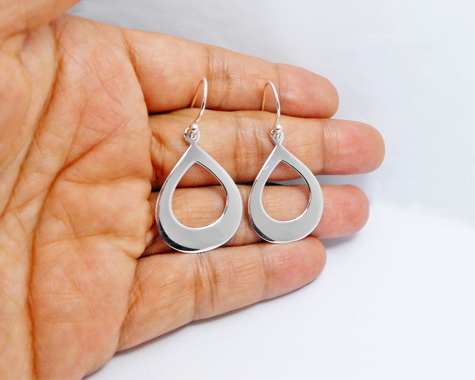 A pair of handcrafted 925 sterling silver elongated oval drop earrings featuring a sleek, high-polished finish, shown held in a hand.